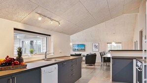 A modern kitchen with a large island, a dining area with a table and chairs, and a view of the outdoors through a window. - Holiday Home in Kappeln (Kappeln)