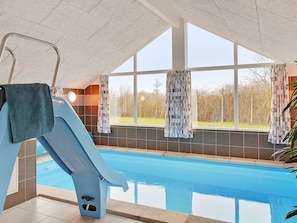 Ein Hallenbad mit Sprungbrett, großen Fenstern und Blick ins Freie.