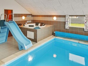 Une piscine intérieure avec un toboggan, un jacuzzi et une fenêtre avec des rideaux.