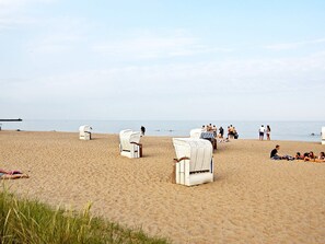 A beach with white wicker chairs and a pier in the background.