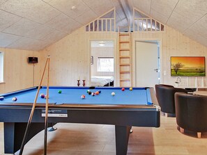 Ein Billardtisch mit Kugeln, eine Billardkeuche und ein Fernseher in einem Raum mit Holzwänden und einem erhöhten Bereich.