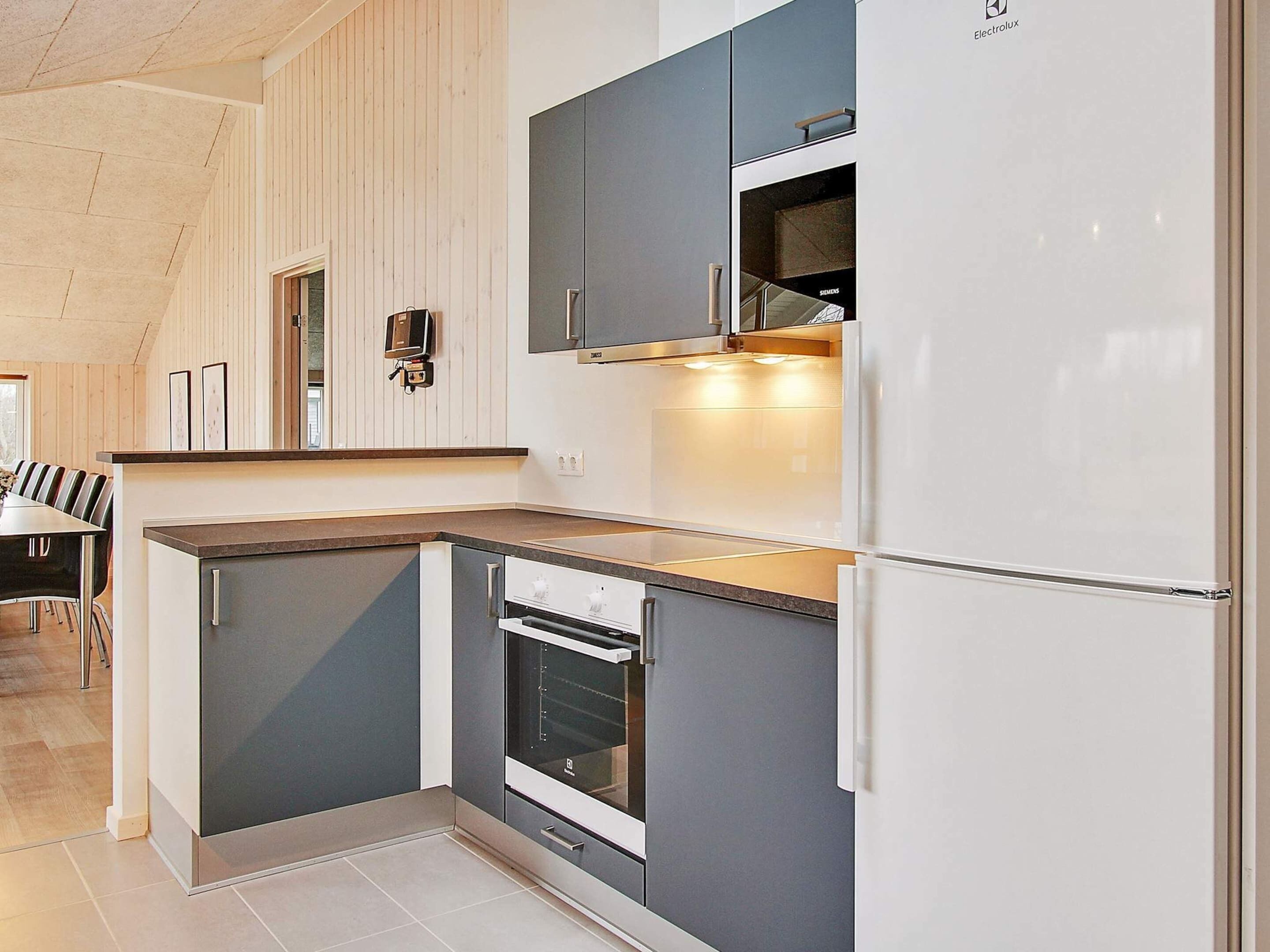 A modern kitchen with grey cabinets, a built-in oven, and a white refrigerator.