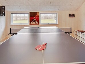 A ping pong table with a net in a room with wooden walls and windows.