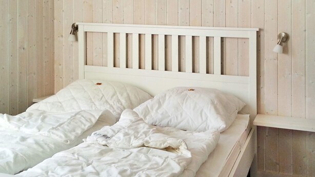 A white bed with a wooden headboard and two pillows, set against a wooden wall. - Holiday Home in Otterndorf (Otterndorf)