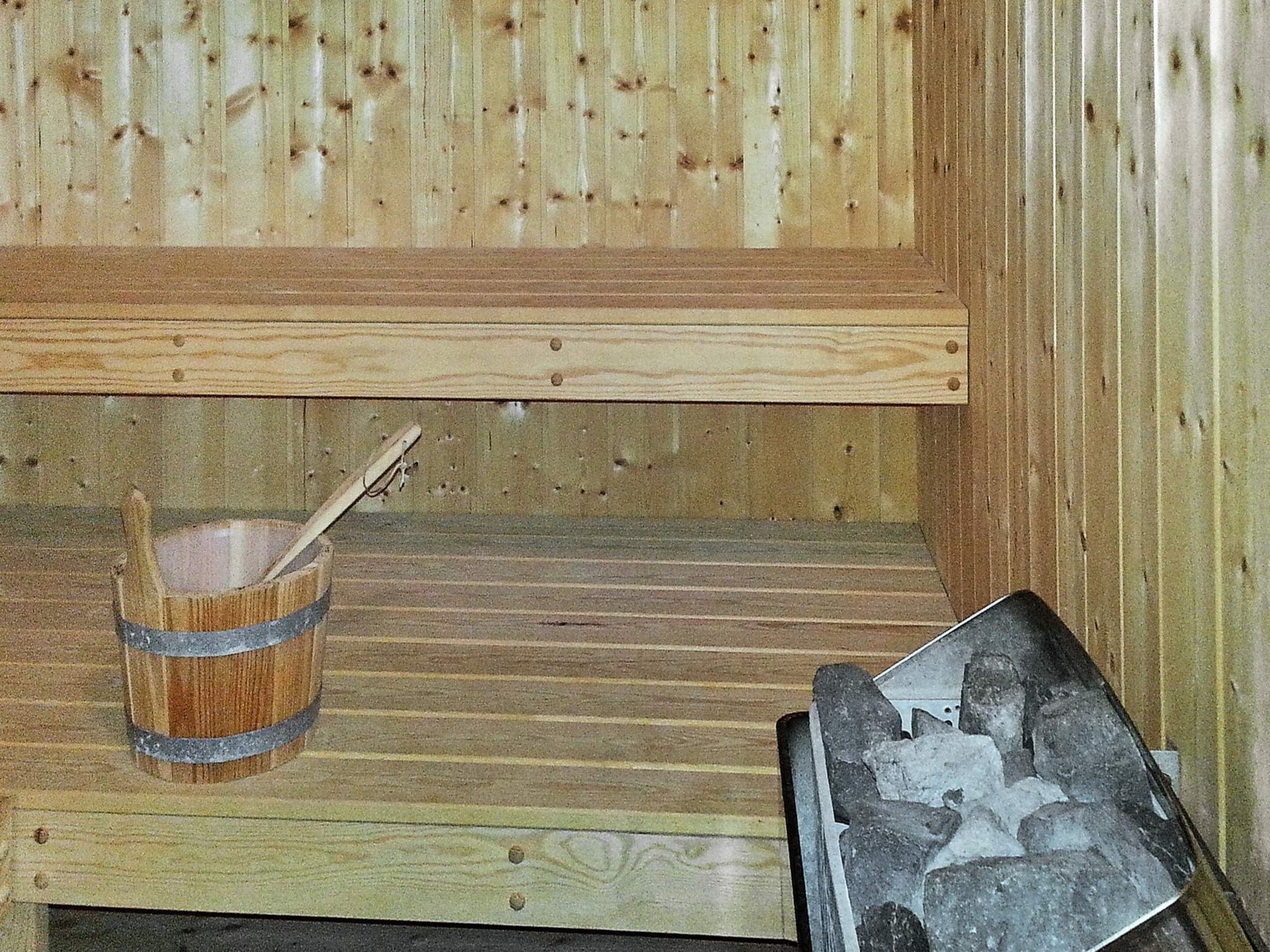 A sauna room with a wooden bench, a wooden bucket with a ladle, and a metal container with stones.