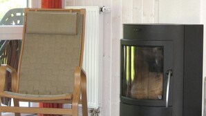 A room with a wooden chair, a black stove, and a window with curtains. - Holiday Home in Otterndorf (Otterndorf)