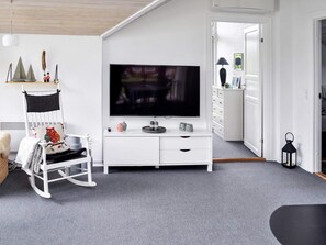 A room with a white entertainment unit, a flat-screen TV, a rocking chair, and a door leading to another room.