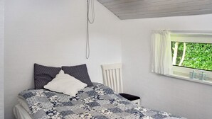 A bedroom with a bed, a nightstand, a window with a view of greenery, and a white headboard. - 4 Star Holiday Home in Struer (Struer)