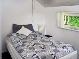 A bedroom with a bed, a nightstand, a window with a view of greenery, and a white headboard.