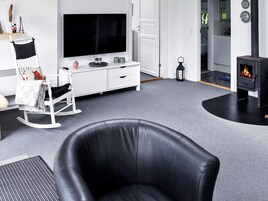 Una sala de estar moderna con un sofá de cuero negro, un mueble blanco para el entretenimiento con televisor de pantalla plana, un estufa de leña negra y una mecedora blanca.