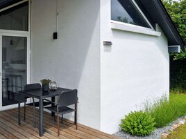 Una casa moderna con un patio, una mesa de comedor con sillas y un pequeño jardín.