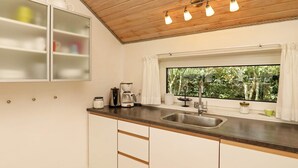A kitchen with a wooden ceiling, a window with a view of greenery, a sink, and a cabinet with a glass door. - 4 Star Holiday Home in Struer (Struer)