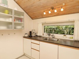 A kitchen with a wooden ceiling, a window with a view of greenery, a sink, and a cabinet with a glass door.