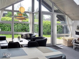 A modern interior with a dining area, a sofa, and a large window offering a view of greenery.
