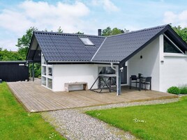Ein modernes Haus mit geneigtem Dach, einer Holzterrasse, einer kleinen Sitzgelegenheit im Freien und einem großen Fenster.