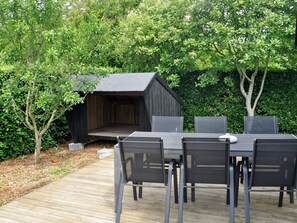 An outdoor dining area with a wooden deck, a table with chairs, and a small wooden structure.