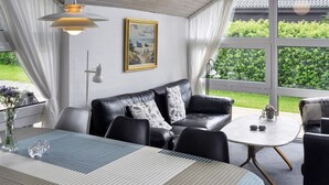 A modern living room with a black leather sofa, a striped table, and a large window offering a view of greenery. - 4 Star Holiday Home in Struer (Struer)