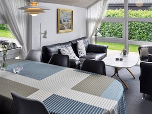 Uma sala de estar moderna com um sofá de couro preto, uma mesa listrada e uma janela grande com vista para vegetação.