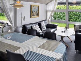 A modern living room with a black leather sofa, a striped table, and a large window offering a view of greenery.