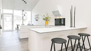 A modern kitchen with a large island, black stools, and a view of the city. - 6 Person Holiday Home in Ringkobing-by Traum (Ringkobing)