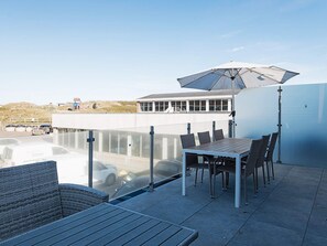 A rooftop terrace with a table and chairs, a large umbrella, and a view of a building and parking area. - 6 Person Holiday Home in Ringkobing-by Traum (Ringkobing)
