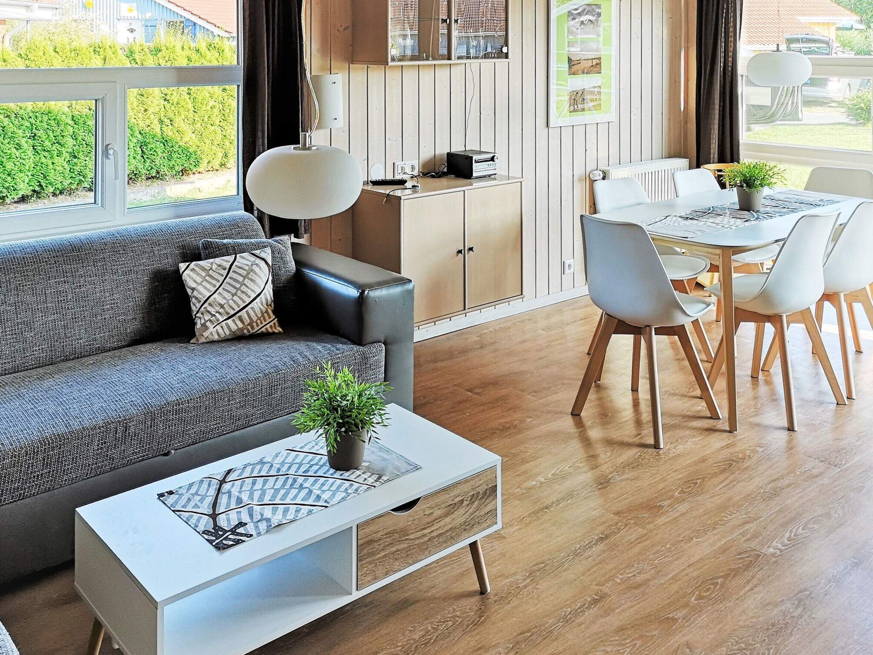 A modern living room with a sofa, coffee table, dining table, chairs, and a kitchen area.