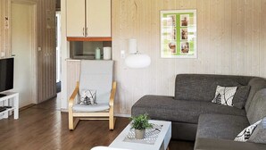 A modern living room with a grey sofa, a white armchair, a small table with a plant, and a television on a stand. - Holiday Home in Otterndorf (Otterndorf)