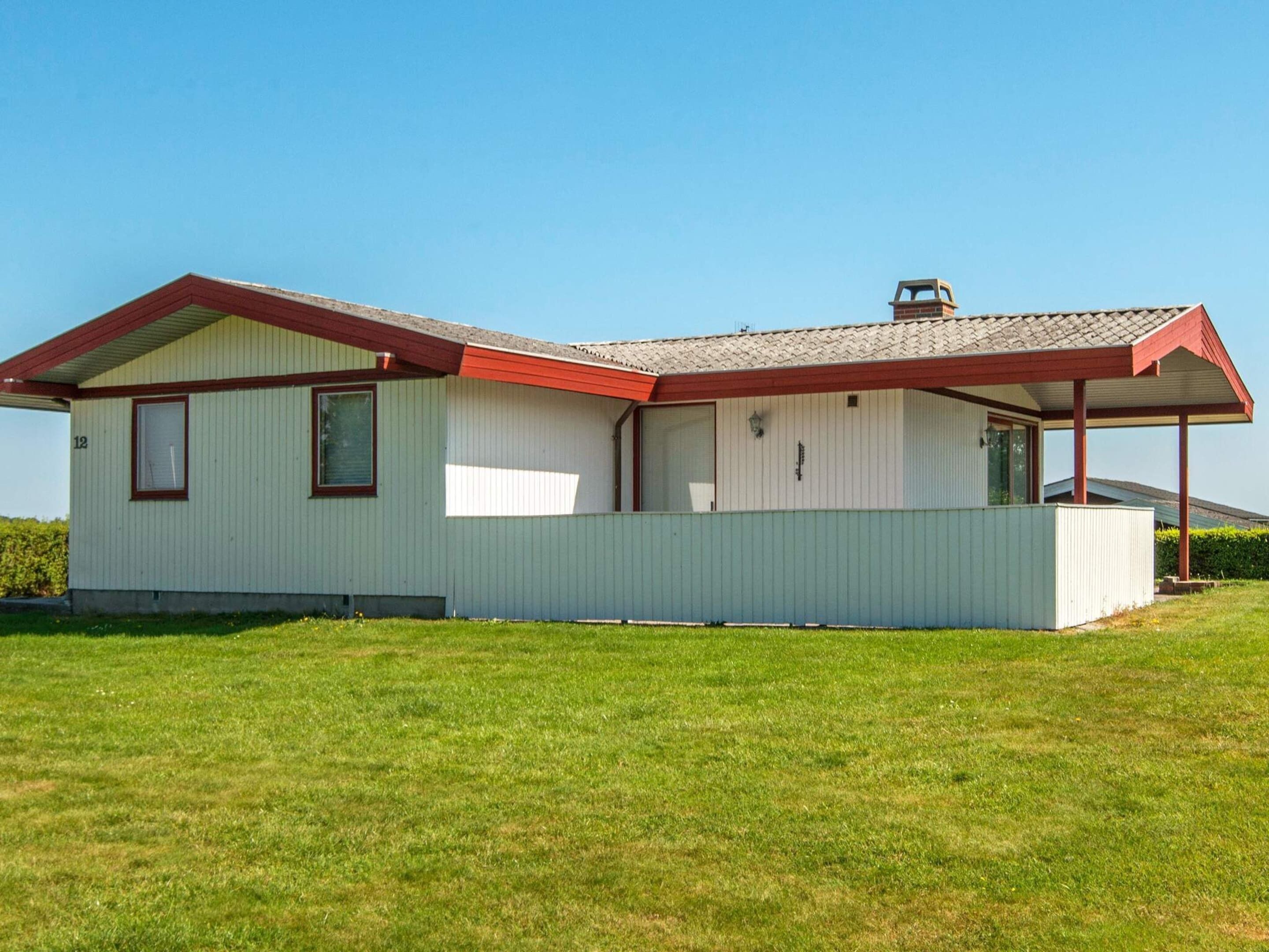 A single-story house with a red roof and white walls, a covered porch, and a grassy yard.