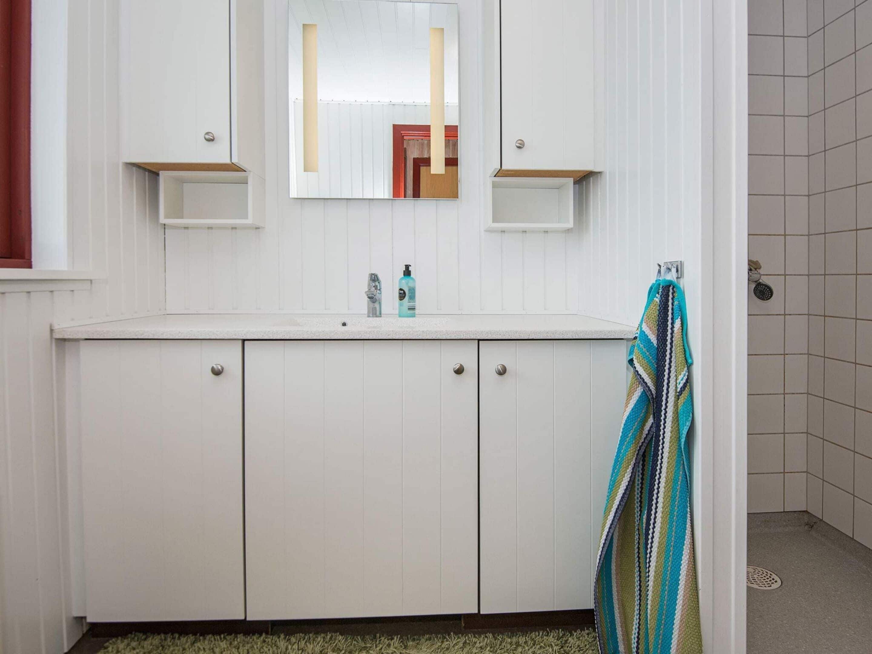 A bathroom with a white vanity, a mirror, two small shelves, a towel rack, and a shower area.