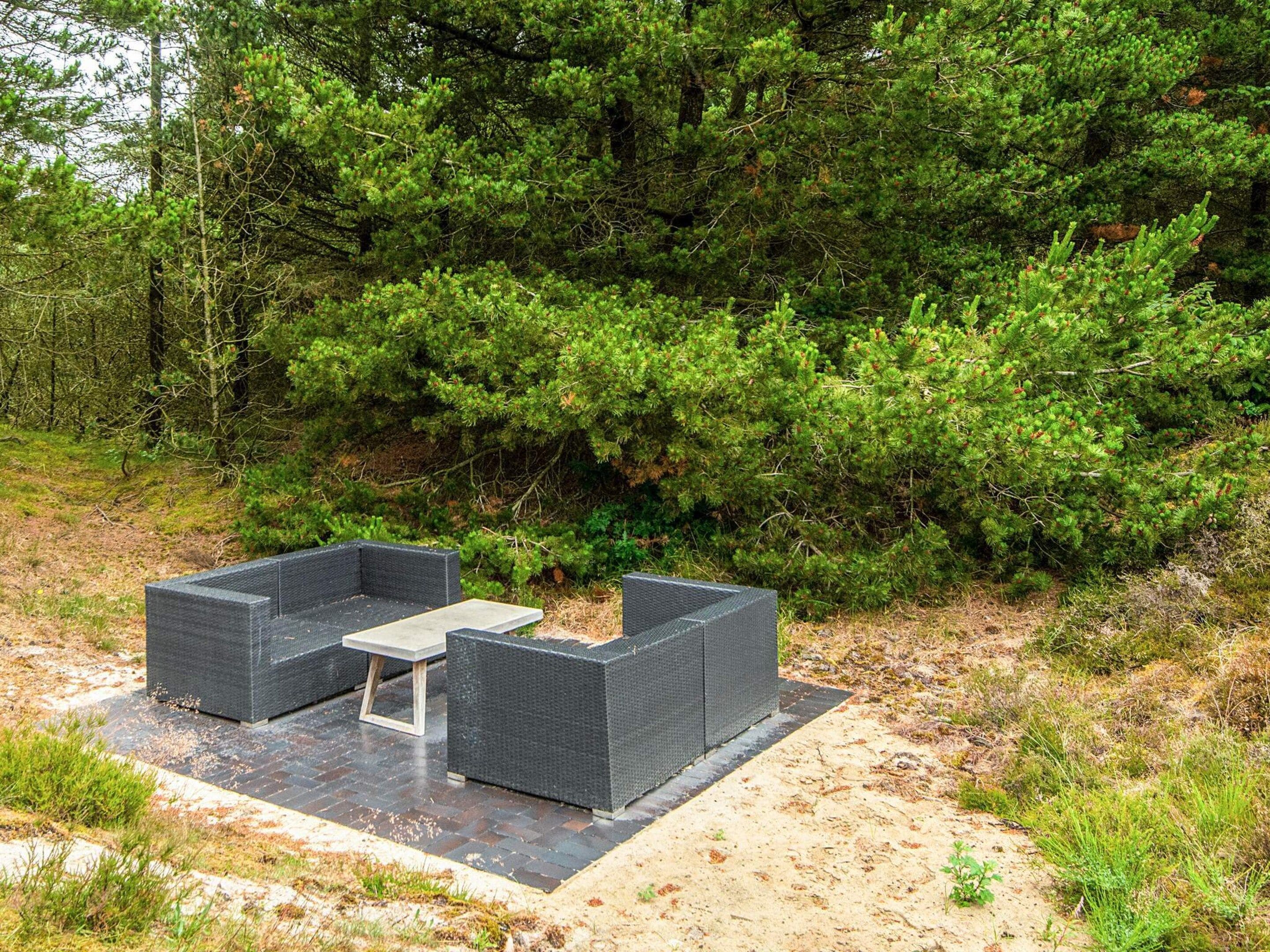 Ein Sitzbereich im Freien mit zwei dunklen Korbschaukeln und einem kleinen Tisch, auf einer gepflasterten Fläche, umgeben von natürlicher Bepflanzung.