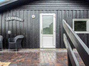 Un bâtiment en bois avec une porte blanche, une enseigne au-dessus de la porte et deux chaises en osier à l’extérieur.