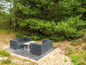 An outdoor seating area with two square tables and chairs, surrounded by dense greenery.