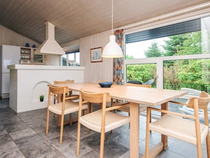 A modern kitchen with a wooden table and chairs, a hanging light fixture, and a view of greenery outside. - 5 Star Holiday Home in Henne (Henne)
