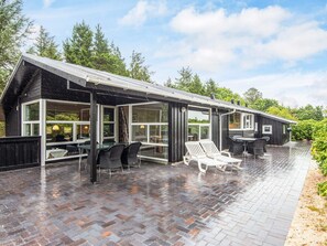 Une maison moderne dotée de grandes fenêtres en verre et d’un patio couvert.