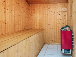 Un sauna avec des murs en bois, un banc et un appareil de chauffage rouge.