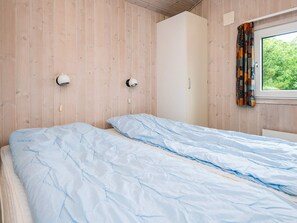 A bedroom with a bed, wooden walls, a wardrobe, and a window with curtains.