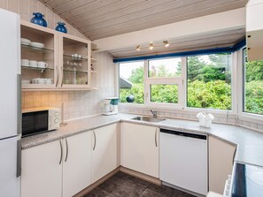 Une cuisine moderne avec des meubles blancs, un lave-vaisselle intégré et une fenêtre donnant sur un espace verdoyant.