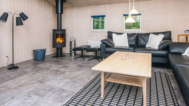 A modern living room with a black leather sofa, a wooden coffee table, a black floor lamp, and a wood-burning stove.