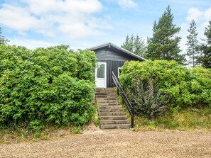 A small, dark-colored cabin with a wooden staircase leading to a white door.