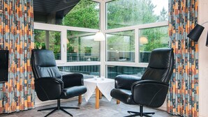 A room with two black leather chairs, a small white table, and large windows with patterned curtains.