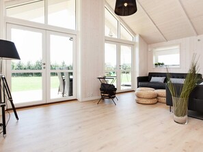 A spacious room with large windows, a black sofa, a small table, and a tripod. - 5 Star Holiday Home in Vaeggerlose (Vaeggerlose)