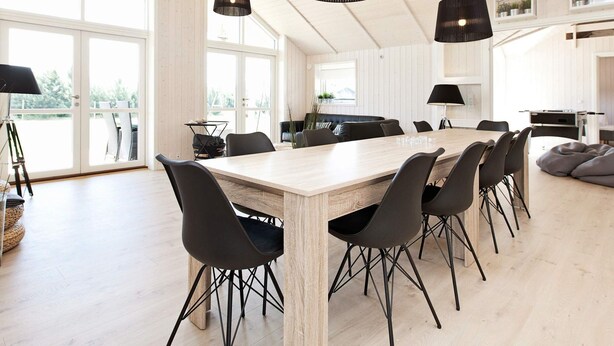 Un comedor amplio con una larga mesa de madera, sillas negras y lámparas colgantes.