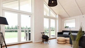 Una habitación amplia con ventanas grandes, un sofá negro, una mesita y un trípode.