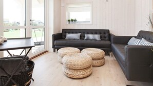Una sala de estar moderna con un sofá de cuero oscuro, otomanas redondas tejidas y un amplio ventanal con vistas al exterior.