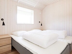 A minimalist bedroom with a bed, a nightstand, and a window. - 5 Star Holiday Home in Vaeggerlose (Vaeggerlose)