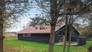 A small, dark blue wooden cabin with a red-tiled roof, surrounded by a grassy yard and trees. - 6 Person Holiday Home in Humble (Sydlangeland)