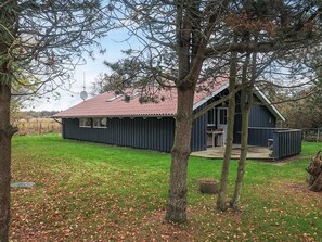 A small, dark blue wooden cabin with a red-tiled roof, surrounded by a grassy yard and trees. - 6 Person Holiday Home in Humble (Sydlangeland)