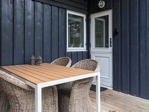 A wooden deck with a table and wicker chairs, a door, and windows. - 6 Person Holiday Home in Humble (Sydlangeland)