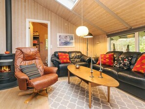 A cozy living room with a leather armchair, a black leather sofa with colorful cushions, a wooden coffee table, and a fireplace. - 6 Person Holiday Home in Humble (Sydlangeland)