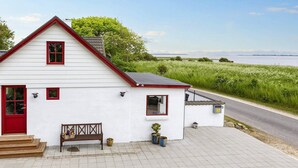 A white house with a red door and windows, a bench, and potted plants on the front porch. - 6 Person Holiday Home in Thisted (Thisted)